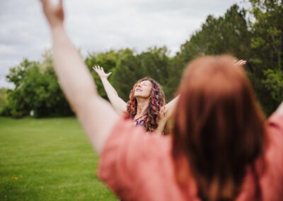 Two women stand outdoors with their arms stretched to the sky.